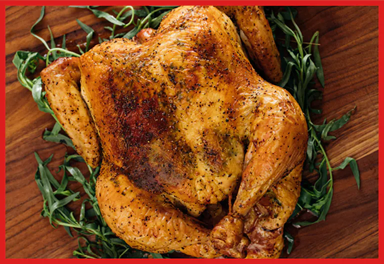 A perfectly roasted whole chicken garnished with fresh herbs, resting on a wooden cutting board.