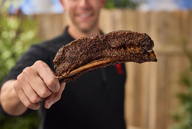 Man holding a bone-in smoked short rib